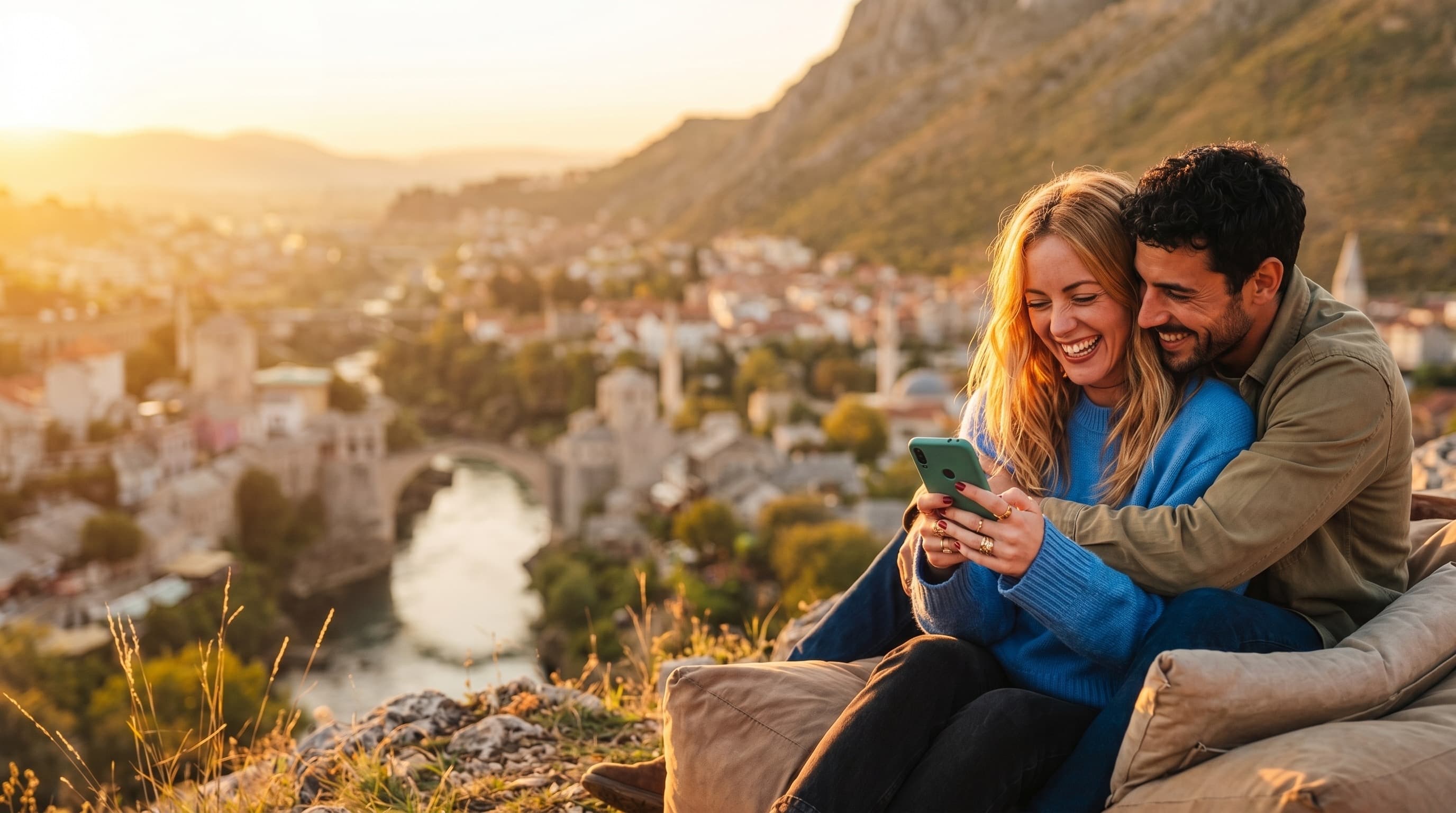 Nasmijani par gleda ponude na telefonu, Stari most u Mostaru u pozadini
